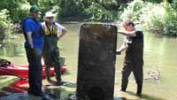 Three people in the river examining a very old refrigerator