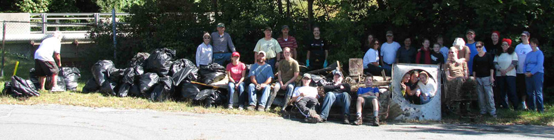 about 30 people standing around a huge pile of trash