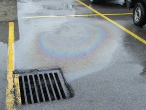 Photo of stormdrain in a parking lot with an oil stain flowing into the drain demonstrating one source of pollution.