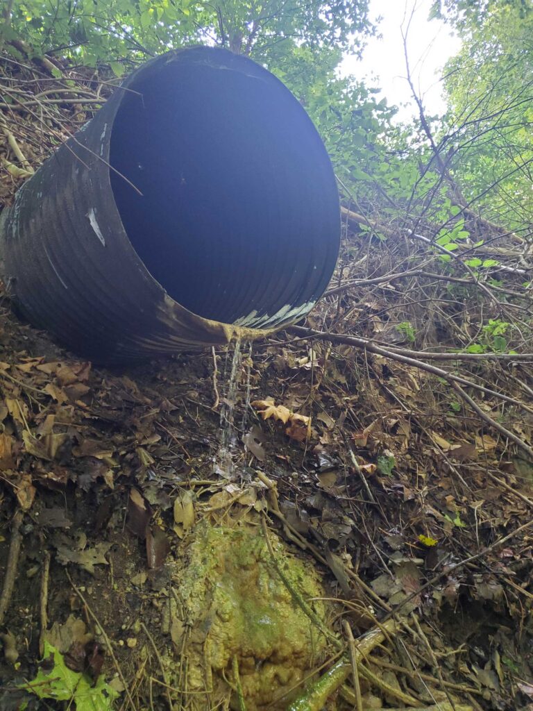Photo of a pipe sticking out of the riverbank with water running from the pipe.